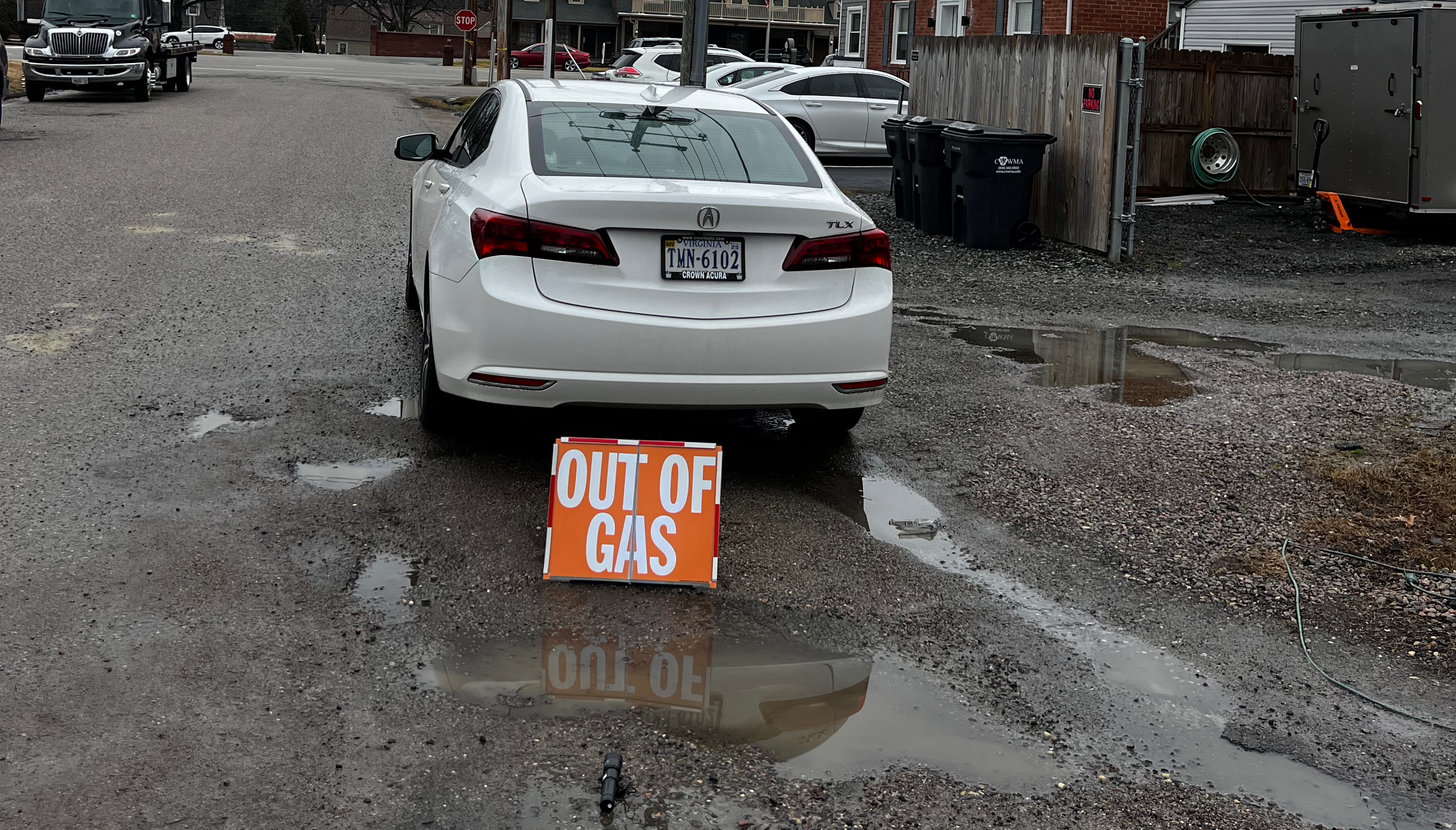 Car with 'Out of Gas' sign on a street with a cloudy sky.