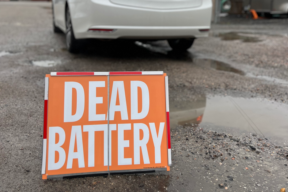Car with a 'Dead Battery' sign in an outdoor setting